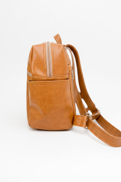 A tan leather backpack bag with a front zip pocket and a top zip closure, shown from a side profile view on a white background.
